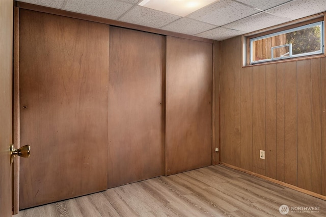 interior space with wooden walls, a drop ceiling, and wood finished floors