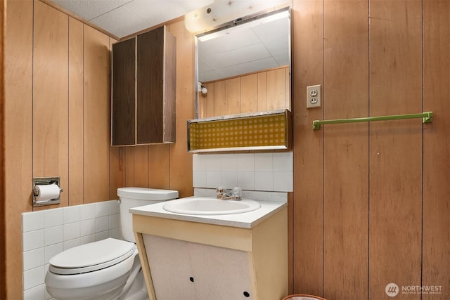 half bathroom featuring vanity, wood walls, and toilet