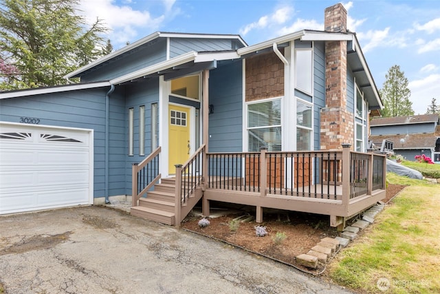 view of front facade featuring a wooden deck, an attached garage, a chimney, and driveway