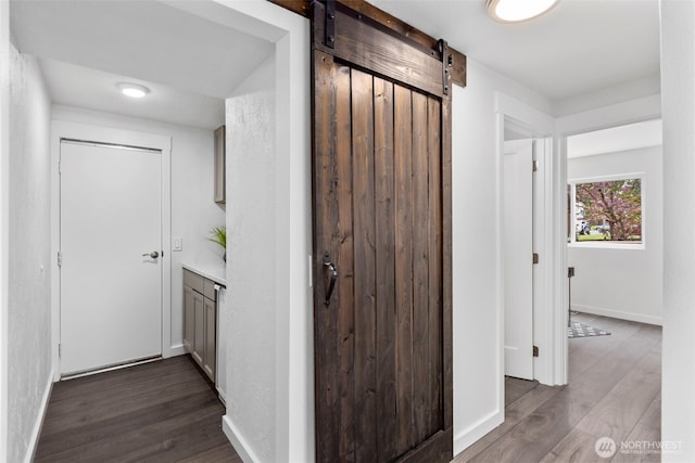 hallway featuring a barn door, baseboards, and dark wood-style floors
