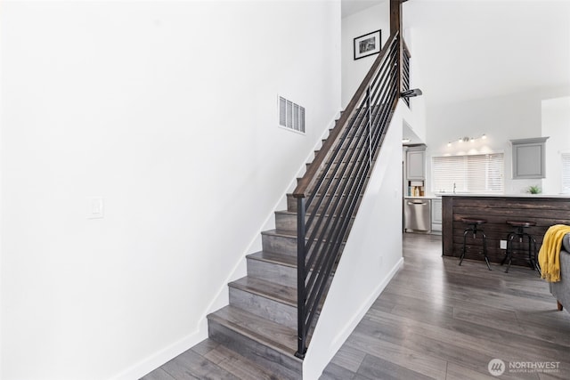 stairway featuring baseboards, wood finished floors, visible vents, and a towering ceiling