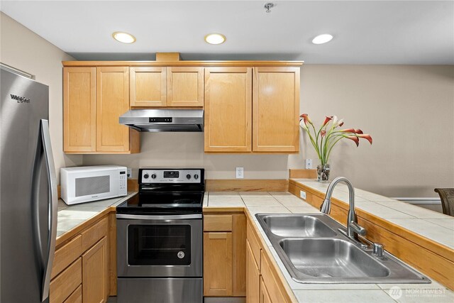 kitchen with light brown cabinets, tile counters, under cabinet range hood, a sink, and stainless steel appliances