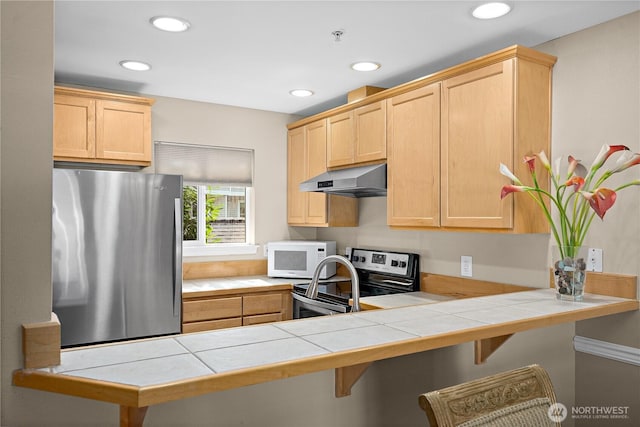 kitchen featuring tile counters, appliances with stainless steel finishes, under cabinet range hood, and light brown cabinetry