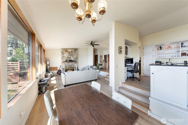12724 Marine Dr, Anacortes, WA 98221 - dining room featuring ceiling fan with notable chandelier, a stone fireplace, and light wood-style flooring