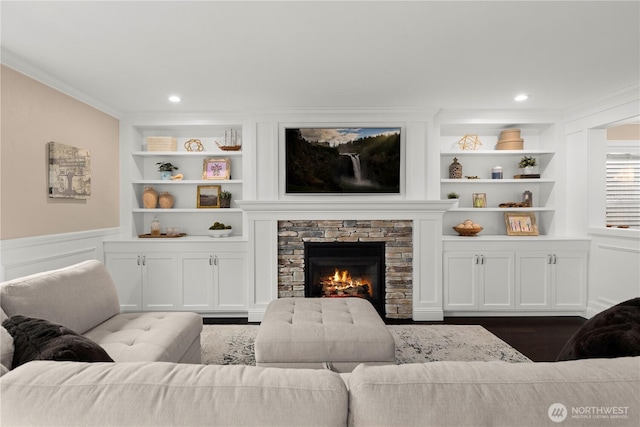 living room featuring built in shelves, crown molding, a wainscoted wall, and dark wood-style floors