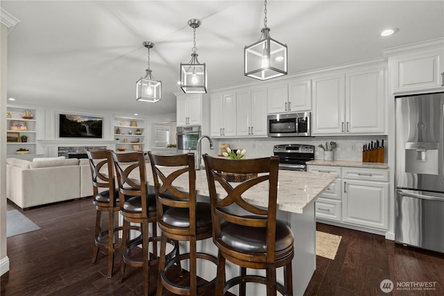 kitchen featuring a kitchen breakfast bar, stainless steel appliances, dark wood-style floors, open floor plan, and white cabinetry