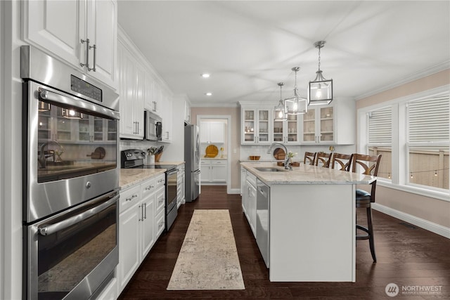 kitchen featuring a sink, an island with sink, glass insert cabinets, white cabinetry, and appliances with stainless steel finishes
