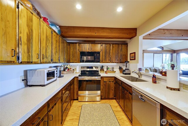 kitchen with appliances with stainless steel finishes, a sink, beam ceiling, brown cabinetry, and light wood-style flooring