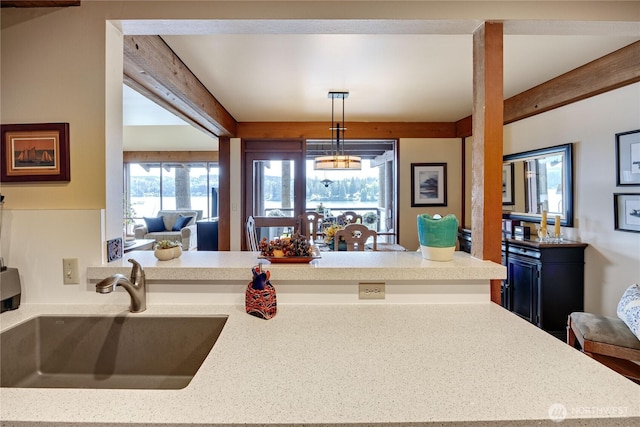 kitchen with a sink, beamed ceiling, a peninsula, pendant lighting, and light stone countertops