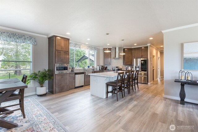 kitchen with tasteful backsplash, a breakfast bar, appliances with stainless steel finishes, wall chimney range hood, and crown molding