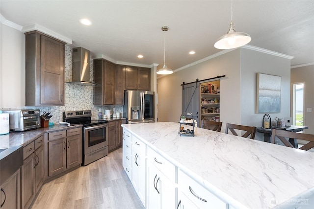 kitchen featuring crown molding, appliances with stainless steel finishes, a barn door, light stone countertops, and wall chimney exhaust hood