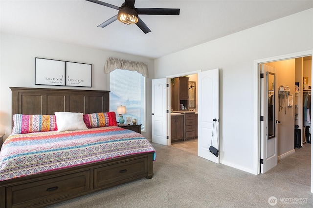 bedroom featuring connected bathroom, ceiling fan, a walk in closet, light carpet, and baseboards