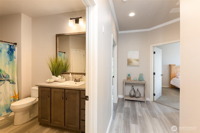 bathroom featuring wood finished floors, backsplash, toilet, vanity, and crown molding