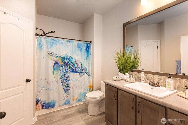 bathroom with wood finished floors, backsplash, toilet, vanity, and shower / tub combo with curtain