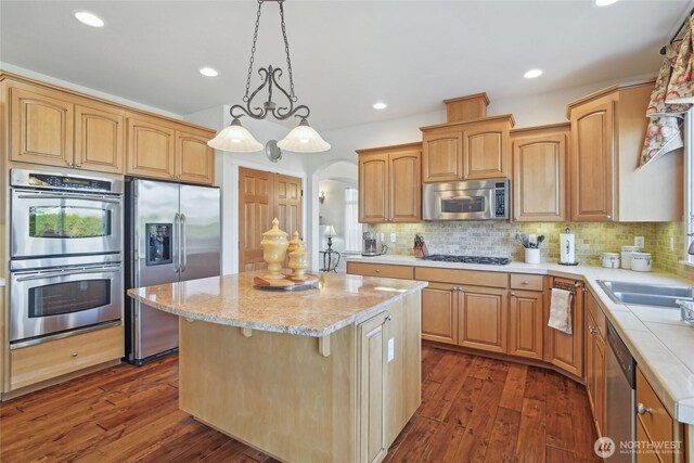 kitchen featuring dark wood finished floors, arched walkways, decorative backsplash, appliances with stainless steel finishes, and a center island