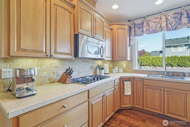 kitchen featuring a sink, tile counters, stainless steel appliances, dark wood-style floors, and backsplash