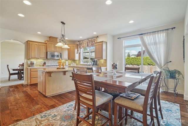 dining space featuring arched walkways, baseboards, dark wood-type flooring, and recessed lighting