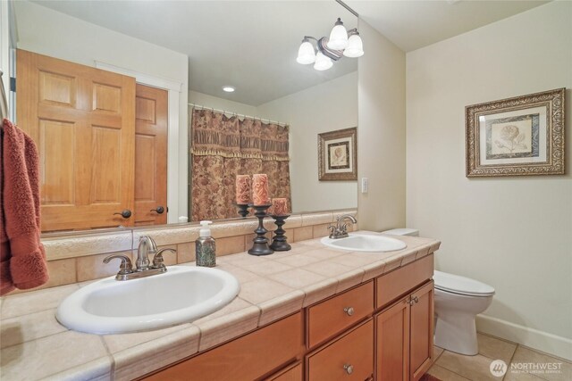 bathroom featuring toilet, double vanity, a sink, and tile patterned floors