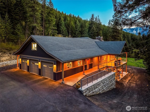 rustic home featuring a wooded view, a shingled roof, a garage, and a chimney