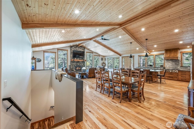 dining room with recessed lighting, lofted ceiling with beams, a stone fireplace, and light wood finished floors