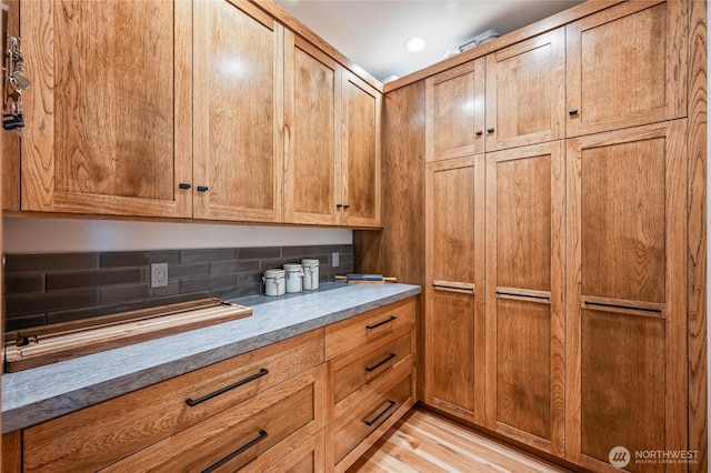 kitchen with light wood-type flooring, brown cabinetry, and backsplash
