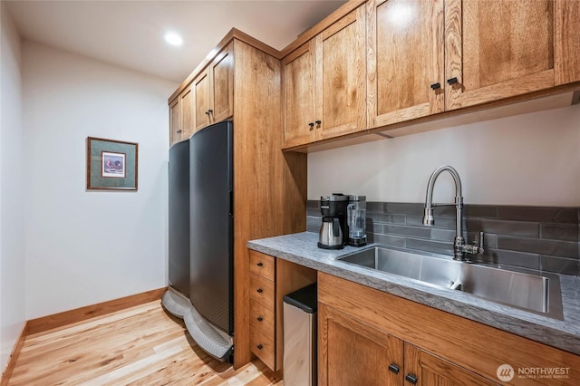 kitchen with fridge, brown cabinets, a sink, baseboards, and light wood-style flooring