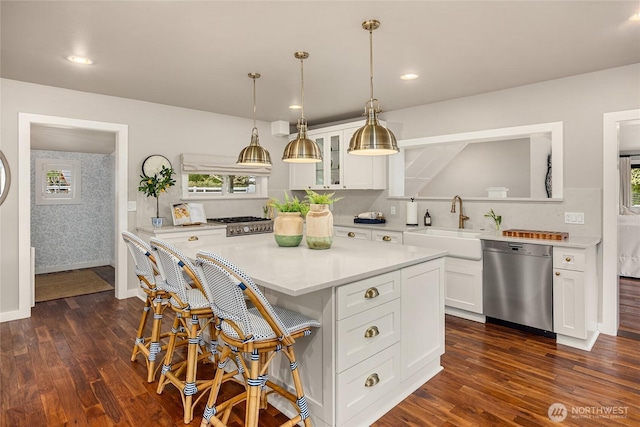 kitchen with dark wood finished floors, stainless steel dishwasher, glass insert cabinets, and a sink