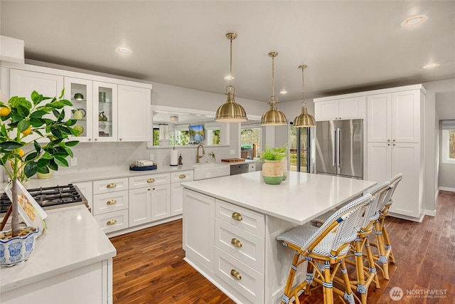 kitchen with a breakfast bar area, a sink, light countertops, recessed lighting, and stainless steel refrigerator