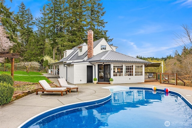 rear view of house with a patio, a sunroom, metal roof, an outdoor pool, and a chimney