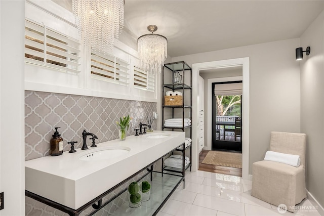 bathroom featuring baseboards, an inviting chandelier, decorative backsplash, and a sink