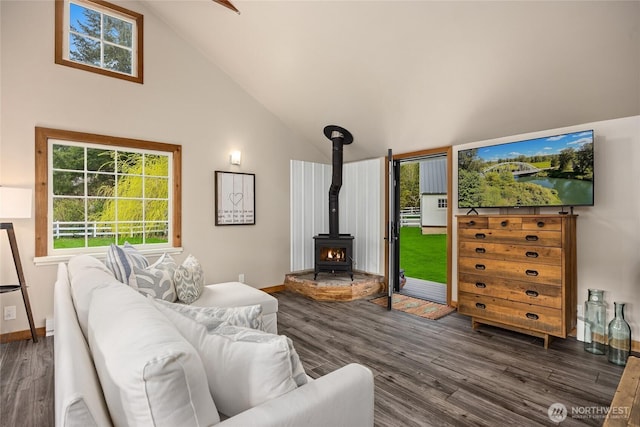 living area featuring a wood stove, high vaulted ceiling, wood finished floors, and a healthy amount of sunlight