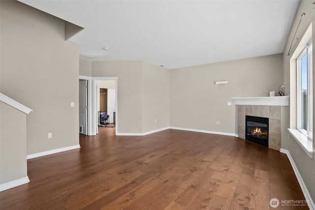 unfurnished living room with a tiled fireplace, baseboards, and wood finished floors