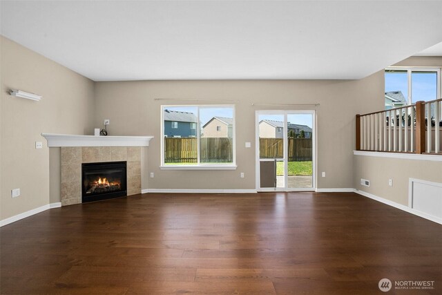 unfurnished living room with a tile fireplace, a wealth of natural light, and wood finished floors