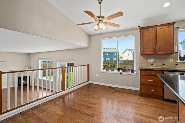 kitchen featuring stainless steel dishwasher, decorative backsplash, wood finished floors, a ceiling fan, and brown cabinetry