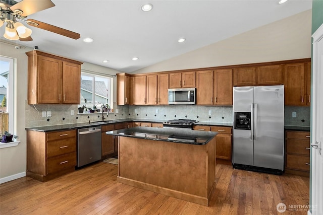 kitchen featuring lofted ceiling, stainless steel appliances, brown cabinetry, and a sink