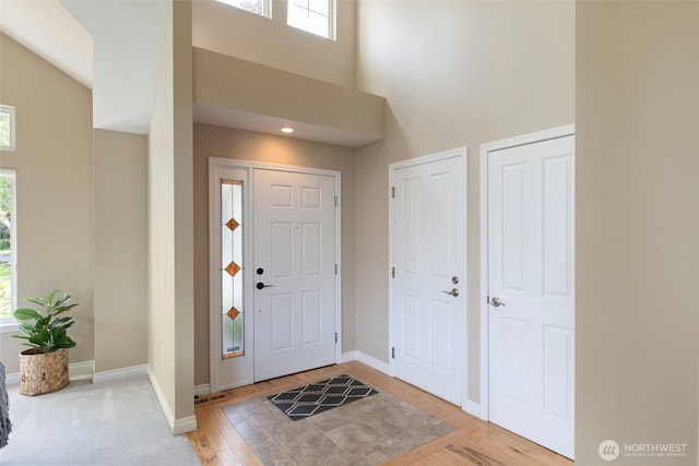entrance foyer featuring a towering ceiling, healthy amount of natural light, baseboards, and light wood-type flooring