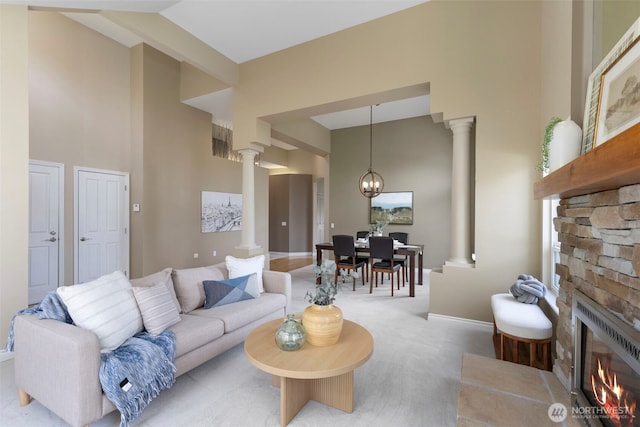 carpeted living room featuring decorative columns, a towering ceiling, a stone fireplace, a chandelier, and baseboards
