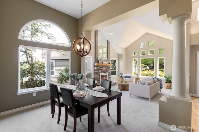 carpeted dining space with ornate columns, high vaulted ceiling, a chandelier, baseboards, and a stone fireplace