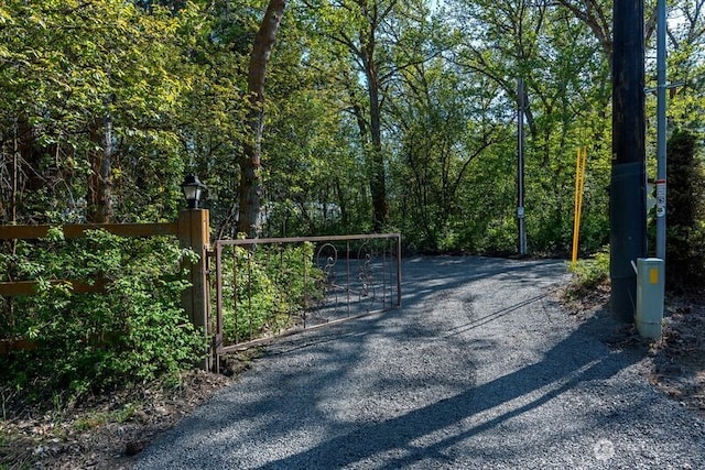 view of road with driveway, a gate, a gated entry, and a wooded view