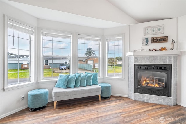 sitting room featuring wood finished floors, a healthy amount of sunlight, a tile fireplace, and vaulted ceiling