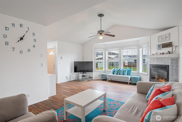 living area with baseboards, vaulted ceiling, a fireplace, wood finished floors, and a ceiling fan