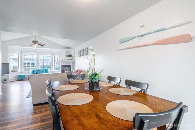 dining area featuring a tile fireplace, ceiling fan, vaulted ceiling, and wood finished floors