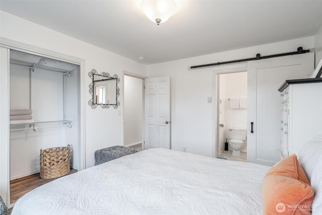 bedroom with wood finished floors, a barn door, ensuite bath, and a closet