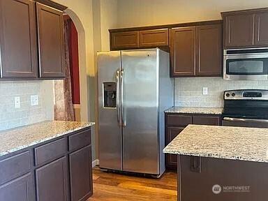 19020 25th Ave E, Tacoma, WA 98445 - kitchen featuring light stone counters, arched walkways, stainless steel appliances, wood finished floors, and tasteful backsplash