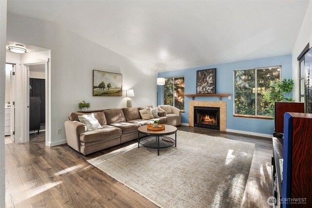 living room featuring vaulted ceiling, a tile fireplace, baseboards, and wood finished floors