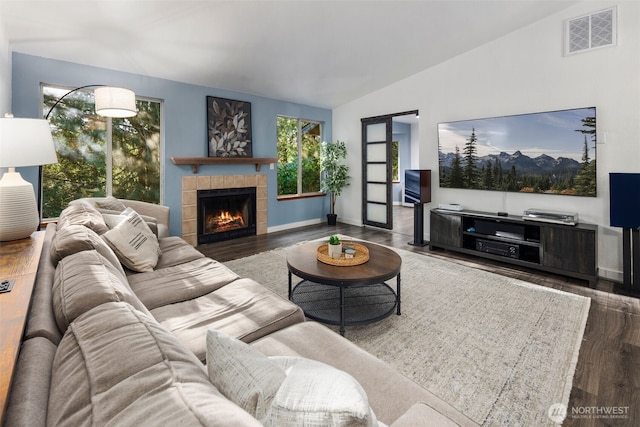 living area featuring a tiled fireplace, visible vents, baseboards, lofted ceiling, and wood finished floors