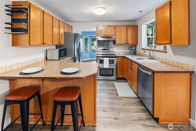 kitchen with under cabinet range hood, open shelves, a sink, a peninsula, and appliances with stainless steel finishes