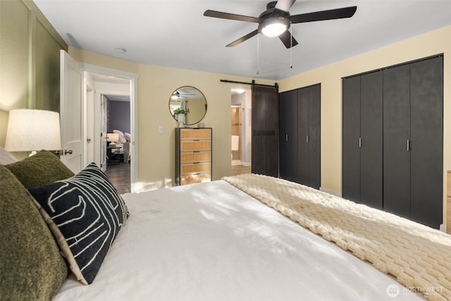 bedroom featuring a barn door, wood finished floors, connected bathroom, two closets, and ceiling fan