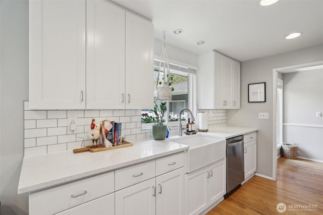 kitchen featuring light wood-style flooring, decorative backsplash, dishwasher, a sink, and white cabinetry