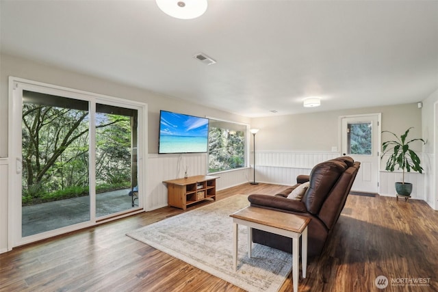 living area featuring wood finished floors, visible vents, a healthy amount of sunlight, and a wainscoted wall